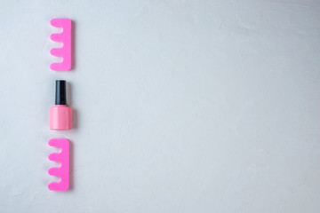 Bottle of pink nail polish and toe separators on a white background on the left. Minimal set of tools that symbolize pedicure. Space for text. Top view