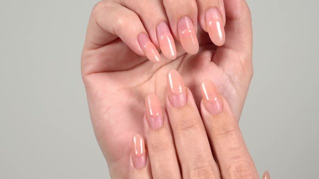 Closeup view video footage of two female hands with old worn long lasting painted nails with pink pastel gel polish.