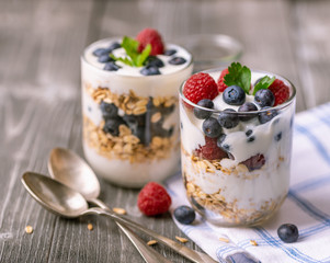 White yogurt in glass jar with fruits on grey background.