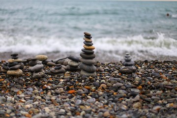 Pyramid of wet stones on a rocky beach against the background of a sea wave