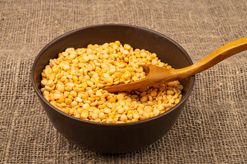 Yellow split peas in a ceramic bowl on a background of coarse-textured burlap. Traditional cereals for making soups and porridge. Close up.