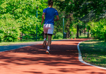 Fototapeta premium Rearview of a young athlete running outdoors on the race track