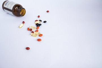 Mix of colorful vitamins and supplements for health and sport in the form of capsules on a white background next to a brown glass jar of vitamins.
