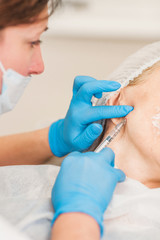 Female doctor makes anti-aging Botox injection in the face of a middle-aged woman for smooth skin