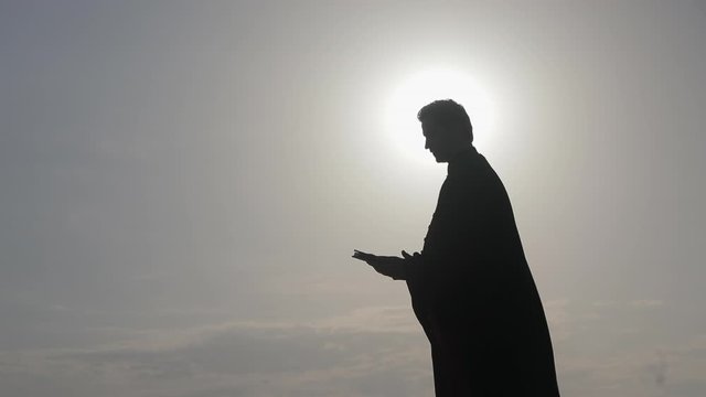 The priest in the mantle reads the Orthodox Bible at the sea, side view.