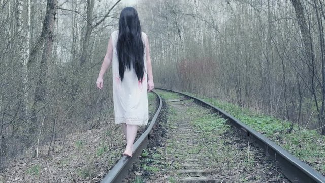 ghost of woman walking in forest along railway track.