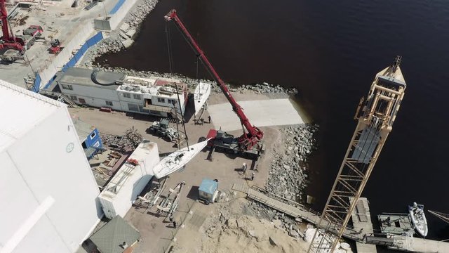 The big industrial crane lifts the sailboat and floats it, the beginning of a season of sailing, drone view point, port Hercules