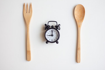 Alarm clock with wood fork and spoon on white bacground. Lunch time. Meal waiting concept.