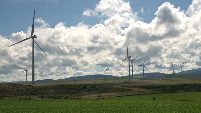 Time lapse of windmills turning through rolling green hills in Idaho as clouds move through the sky.