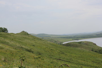 Panoramic view. A lagoon with a clean mountain lake in the midst of majestic mountains in a haze of fog. Green grass. 