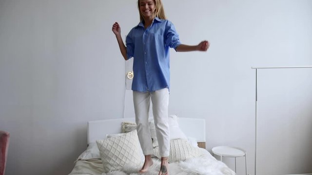 Young attractive caucasian woman jumping on bed in in a luxury light apartment.