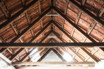 Looking up at the ceiling of an old barn with old roof tiles and wooden beams