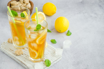 Ice tea with lemon, brown sugar, mint leaves and ice cubes in a glass on a board on a light background. Summer refreshing drink. Horizontal orientation, copy space.