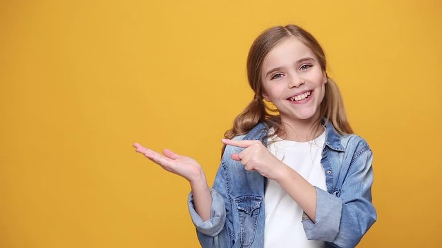 Little fun teen kid girl 12-13 years old in denim jacket white t-shirt posing isolated on yellow background studio People childhood lifestyle concept Smiling showing pointing fingers hand on workspace