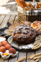 Concept of homemade bread, natural farm products, domestic production. Healthy and tasty organic food. Bread, eggs, flour. Wheat spica as decor. Closeup, wooden background