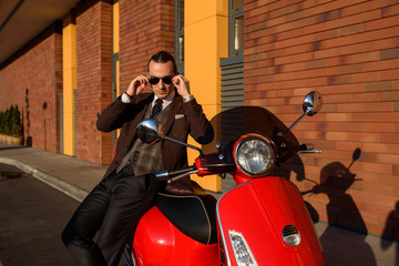 Fototapeta na wymiar Youman man in elegant suit is leaning on a red vintage scooter motorbike