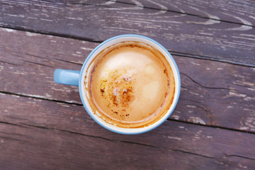 A blue cup of cappuccino on a background of old brown wood with peeling paint. Close-up. View from above.