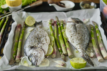 fresh baked dorado fish on a baking sheet with asparagus and lime