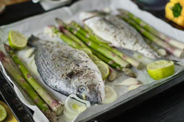 fresh baked dorado fish on a baking sheet with asparagus and lime