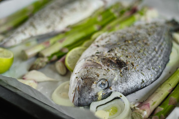 fresh baked dorado fish on a baking sheet with asparagus and lime