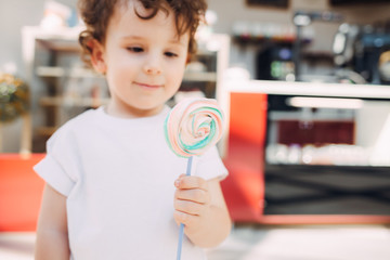 A curly-haired boy with a lollipop on a sunny day.