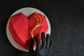 Heart shaped cake. angular red mousse cake on a dark stone table. Confectioner decorates a cake top...