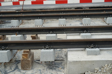 Metal rails attached on conrete boocks ready to be installed on a civil engineering construction site. Building of a new tram line, bordered by barrier planks in red and white. 