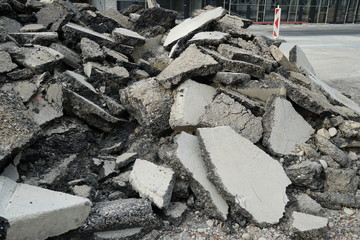 Pieces or clumps of asphalt or bitumen from a dismantled road cover on a big pile with vertical construction barrier on a civil engineering building site