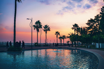 Limassol , Cyprus. Silhouettes of palms and walking tourists people on Molos Park at background of...