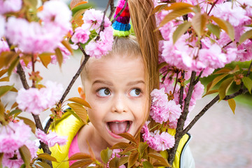 Obraz na płótnie Canvas Cute child girl holding sakura blossom. Funny face. Comic grimace, funny emotion, crazy facial.