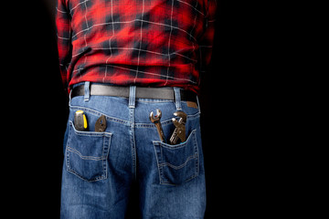 a man in blue denim jeans and a red plaid shirt with pliers and tools in the rear pockets on black