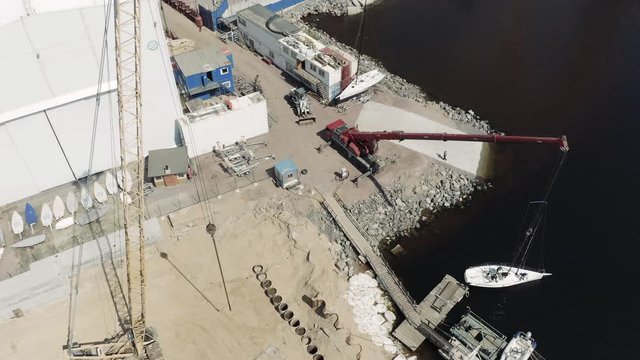The big industrial crane lifts the sailboat and floats it, the beginning of a season of sailing, drone view point, port Hercules