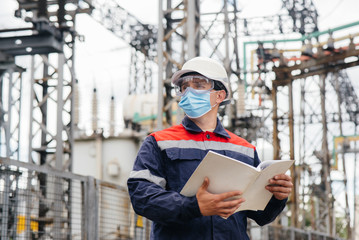 An electrical substation engineer inspects modern high-voltage equipment in a mask at the time of...