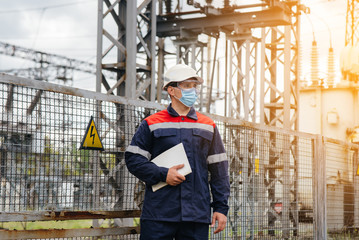 An electrical substation engineer inspects modern high-voltage equipment in a mask at the time of...