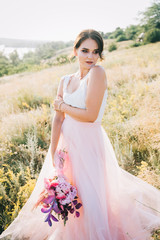 Fototapeta na wymiar Bride in a luxurious white and pink wedding dress in nature at sunset