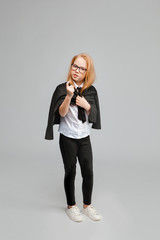 Cute red-haired girl in a business suit looks sternly and points a finger