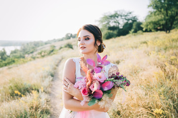 Bride in a luxurious white and pink wedding dress in nature at sunset