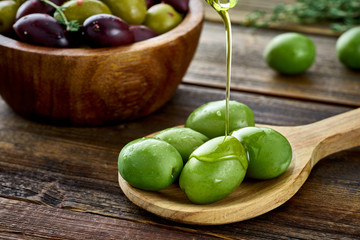 Olive oil pouring on big green olives. Kalamata olives lying in a wooden bowl on the background. Food photography