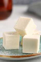 Cubes of vanilla pastila (marshmallows) with a cup of black tea, low-calorie dessert closeup.