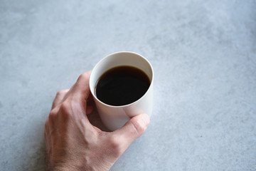 Cup of black coffee in a handmade white ceramics mug, white marble background. Man hands shown.