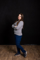 Portrait of a young beautiful full-length girl on a black background in the apartment. slate wall in the background. woman in a gray sweater, jeans and sneakers. European appearance.