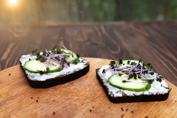 two sandwiches with cucumber and red cabbage micro-greens on a wooden tray. green bokeh on the background. healthy eating. serving option.