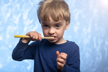three year old child brushes his teeth with a bamboo toothbrush in the bathroom on a blue texture background. horizontal photo. environmentally friendly. morning hygiene concept.