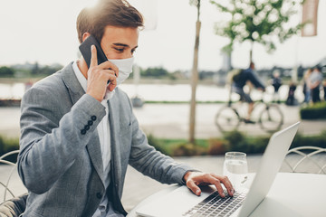 Young man wearing a face mask talking on a phone and working on a laptop - Powered by Adobe