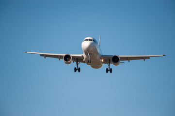Airplane approaching an airport with landing gears down and landing lights on.