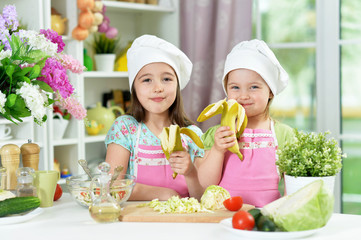 Cute girls eating bananas together in kitchen at home