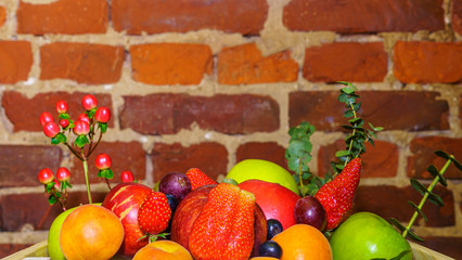 Set of berries and fruits in wooden box. Apple, strawberry, grape, berry and peach on a red brick...