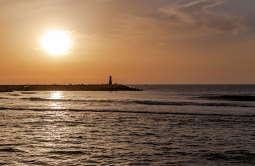 Fototapeta na wymiar Stone breakwater with a small lighthouse in the Mediterranean at sunset