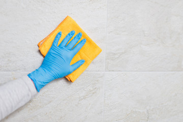 Close up of female hand in protective surgical glove washing ceramic tiles in bathroom with microfiber cloth.