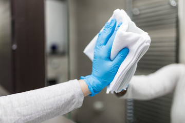 Close up of female hand in rubber glove polishing mirror with rag. Housekeeping and cleaning service.